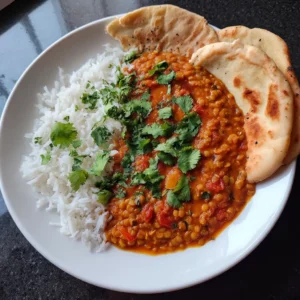 A vibrant plate of Vegan Lentil Curry served with fluffy white rice and golden naan bread, garnished with fresh cilantro.