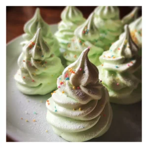 Meringue Christmas Tree Cookies 2 Delicate pastel green Christmas tree meringues, spiraled and topped with colorful sprinkles, presented on a light serving plate, ideal for a Christmas tree meringues recipe.