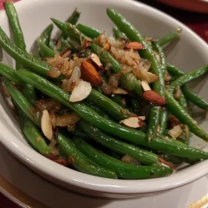 A close-up of a vibrant Christmas green beans recipe garnished with caramelized onions and almonds in a white bowl.