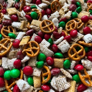 A vibrant overhead shot of a festive Christmas trash recipe mix with red and green M&M's, pretzels, and white-coated cereal.