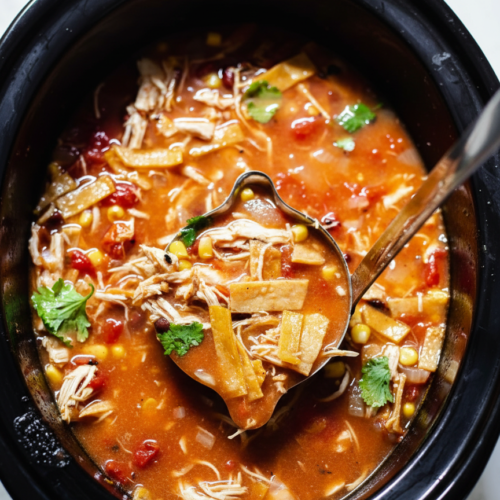 Thick crockpot chicken tortilla soup in a ceramic bowl on white marble, showing the velvety texture from a masa harina slurry.