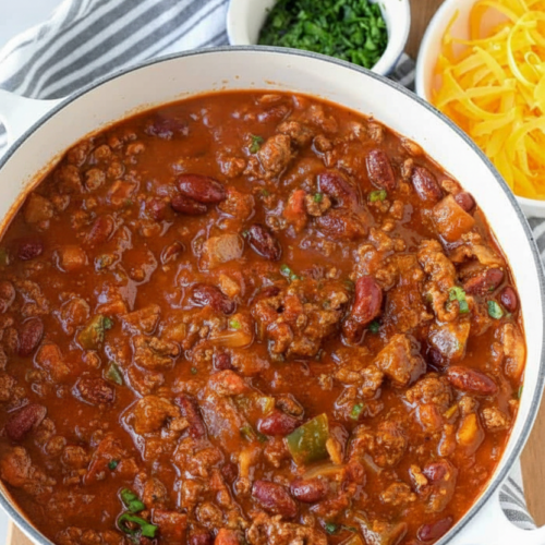 A homemade chili recipe in a minimalist ceramic bowl on white marble, showing rich cocoa-tinted beef and kidney beans.