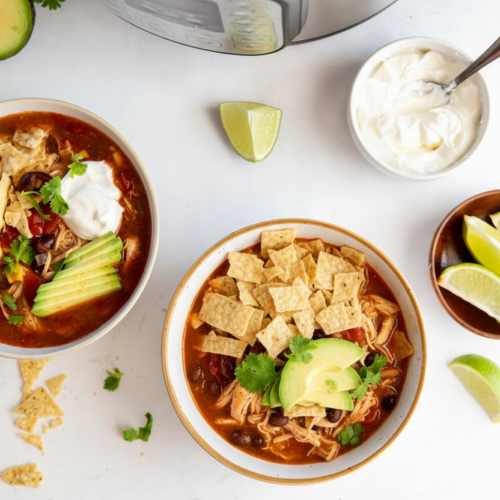 Instant pot chicken tortilla soup in a minimalist ceramic vessel on white marble, thickened with toasted tortillas.