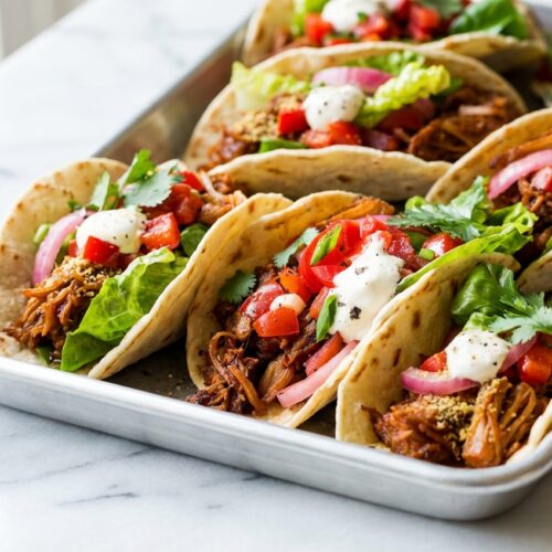 Seared Jackfruit Tacos with a nutritional yeast and coconut oil umami infusion on a white marble surface in natural light.