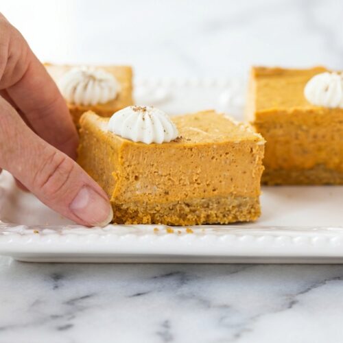 Pumpkin Cheesecake Bars with a brown butter crust on a white marble surface in soft natural window light.