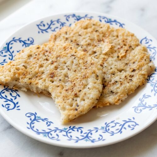 Rice cake recipe with a golden umami-parmesan crust on a minimalist ceramic plate over a white marble surface.