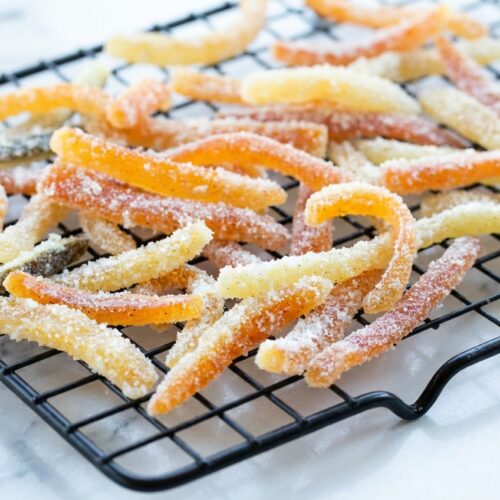 Glistening candied orange peel with vanilla bean specks and sea salt on a white marble surface in natural light.
