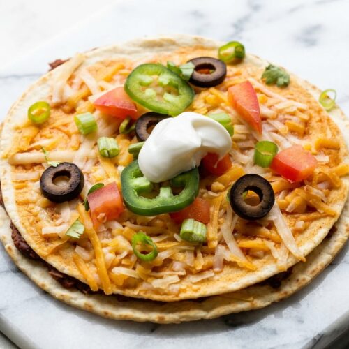 Vegan Mexican Pizza with a golden double-crisp umami shell on a white marble surface under natural window lighting.