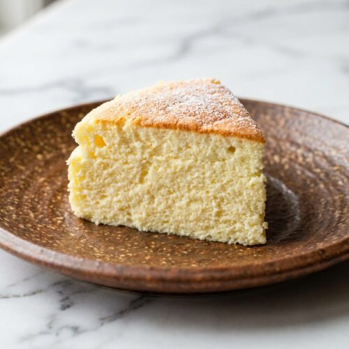 Golden 3 Ingredient Yogurt Soufflé Cake with stiff peaks on white marble, featuring a light and airy texture.