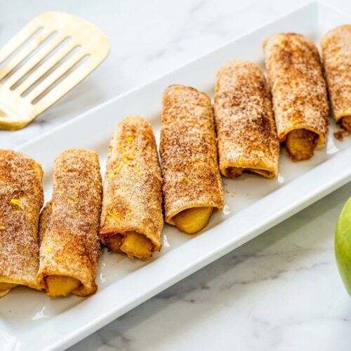 Golden Air Fryer Apple Pie Taquitos on white marble, seasoned with lemon zest and sea salt for a zesty twist.