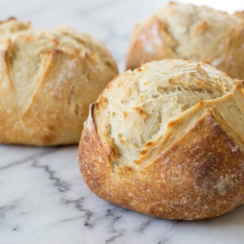 Artisan Bread Recipe (4 Ingredients) with a blistered, golden crust from a cold-fermentation finish on a white marble surface.