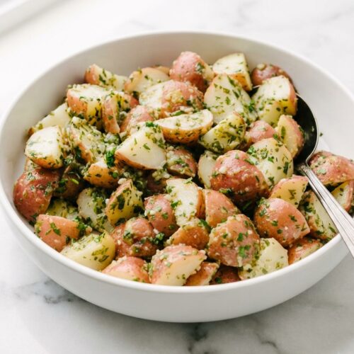 Authentic Italian Potato Salad with a silky starch-emulsion vinaigrette in a minimalist ceramic vessel on white marble.