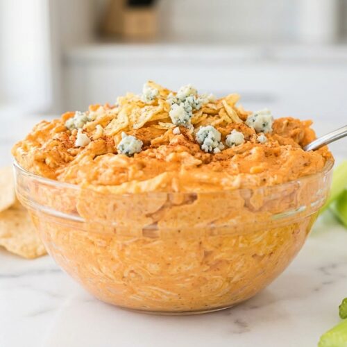 Buffalo chicken dip crock pot with smoky kettle chip crust and blue cheese crumbles on white marble, soft shadows.