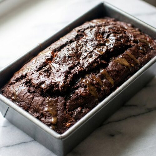 Chocolate Banana Bread with a brown butter espresso glaze on a white marble surface with natural window lighting.