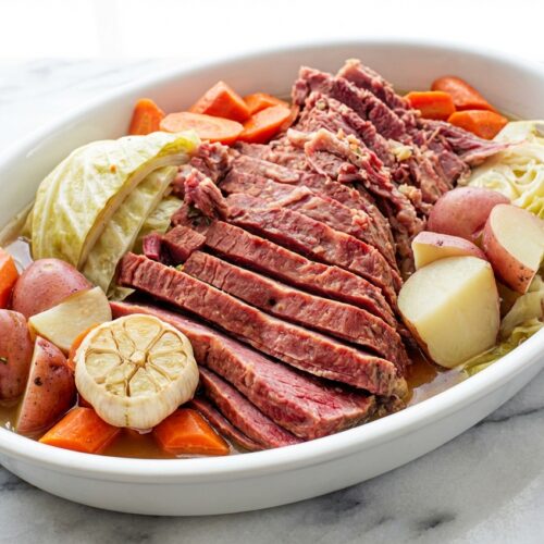 Corned beef recipes slow cooker brisket with halved garlic and cider vinegar on white marble.