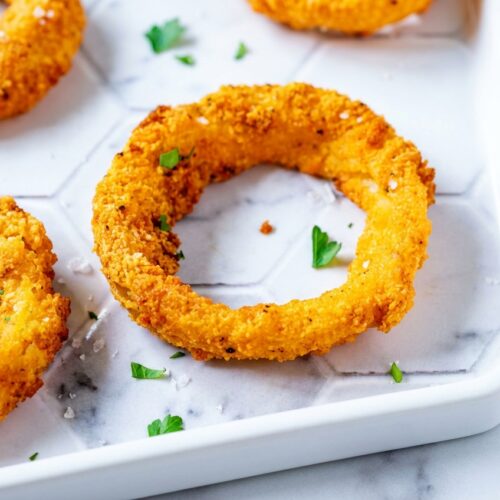 Crispy Keto Onion Rings on a white marble surface, double-dredged with whey protein isolate for a golden Maillard reaction.
