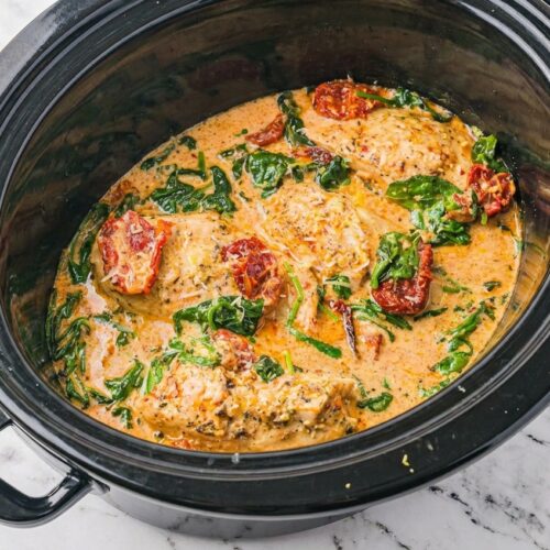 Creamy crockpot tuscan chicken recipe topped with fresh lemon zest in a minimalist ceramic bowl on a white marble surface.