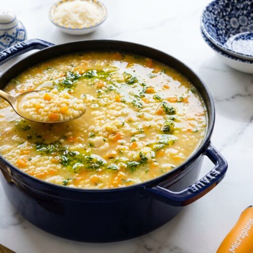 Creamy italian pastina soup in a minimalist ceramic vessel on white marble, drizzled with vibrant lemon-thyme gremolata oil.
