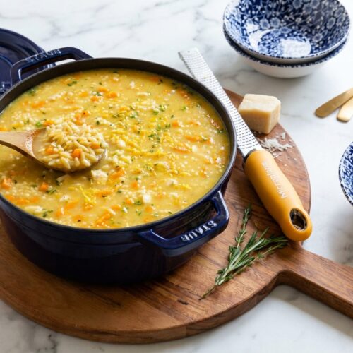 A minimalist ceramic bowl of italian penicillin soup on a white marble surface with toasted pastina and lemon zest.