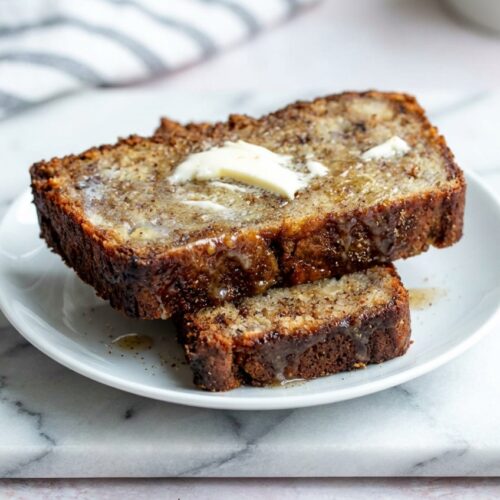 Moist Banana Bread with brown butter and toasted cardamom on a minimalist ceramic plate over a white marble surface.