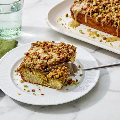Pistachio Coffee Cake on a minimalist ceramic plate, featuring a golden toasted brown butter streusel topping and moist crumb.