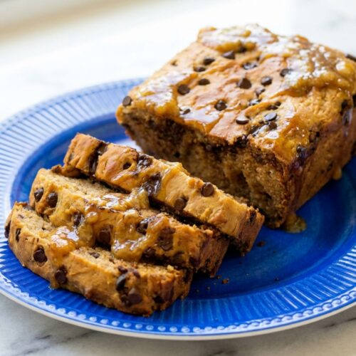 Sliced Protein Banana Bread on a white marble surface with a golden crust, featuring a moist crumb swirled with caramelized banana mash and brown butter.