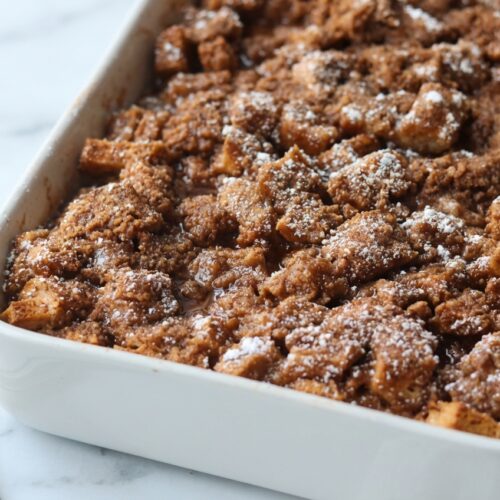 Sourdough French Toast Casserole topped with a golden brown butter and cardamom infused streusel on a white marble surface.
