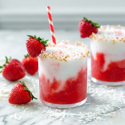 Strawberry Coconut Daiquiri in a hurricane glass with a toasted coconut and Himalayan sea salt rim on white marble.