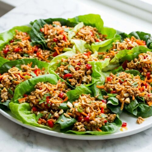Thai Lettuce Wraps with minced lemongrass and crispy fried shallots on a minimalist ceramic plate over a white marble surface.