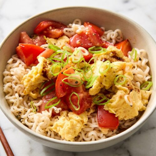 Al dente tomato and egg pasta with a tomato paste bloom in a ceramic bowl on white marble with soft shadows.