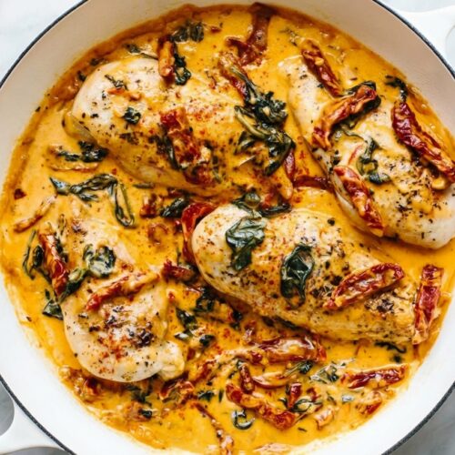 Golden chicken breast cutlets in a creamy sauce with sun-dried tomatoes and spinach on a white marble surface. Tuscan chicken recipe featuring a parmesan rind and smoked paprika infusion.