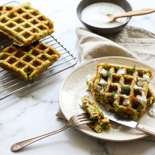 Crispy broccoli cheese waffles with a golden parmesan frico crust on a white minimalist plate, soft natural window light.