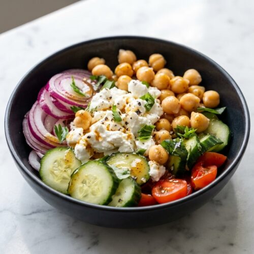 Chickpea & Cottage Cheese Power Salad in a minimalist ceramic bowl on a white marble surface with warm-infused spiced dressing.