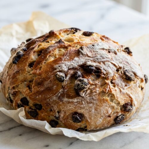 Cinnamon Raisin Artisan Bread with plump tea-soaked raisins on a white marble surface under natural lighting.