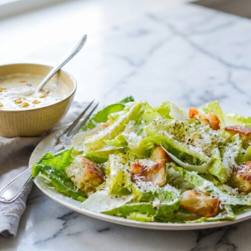 Creamy caesar salad dressing recipe with roasted garlic and miso maceration in a minimalist ceramic bowl on white marble.