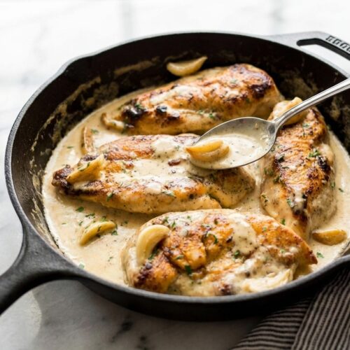 Flat lay of Creamy Garlic Chicken with Dijon-Thyme emulsion in a minimalist ceramic vessel on white marble.