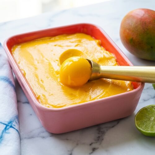 Smooth scoops of mango sorbet recipe in a minimalist ceramic vessel, featuring a creamy texture from liquid glucose.