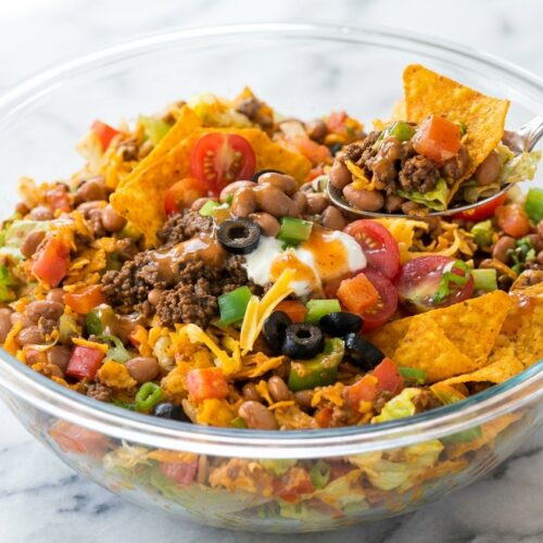 Dorito Beef Taco Salad in a minimalist white ceramic bowl on marble, drizzled with zesty lime-chipotle Catalina emulsion.
