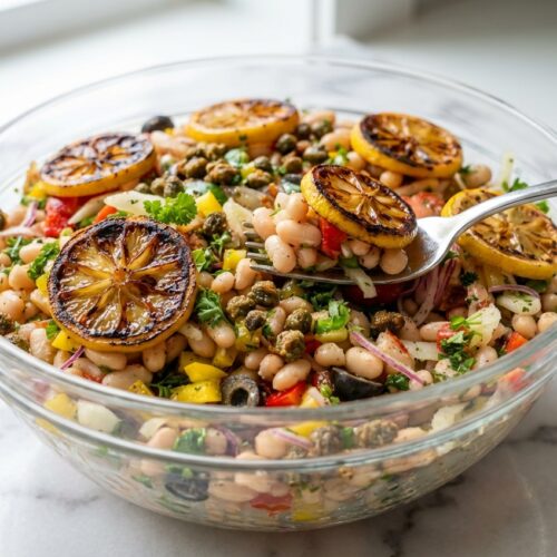Italian White Bean Salad in a minimalist white ceramic bowl on marble, topped with charred lemon and fried capers.