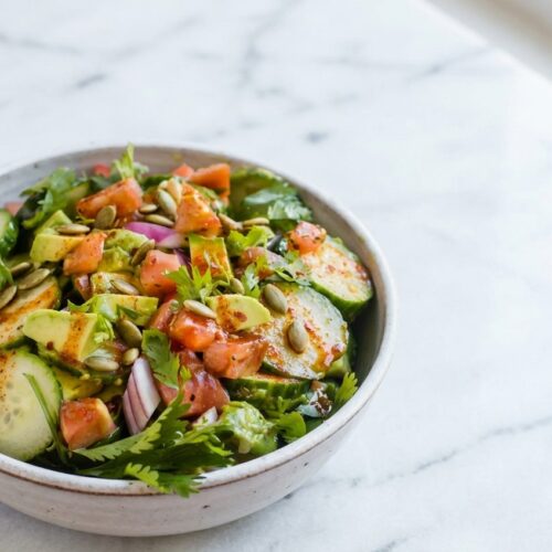 Keto Avocado Salad in a minimalist ceramic bowl on white marble, topped with toasted pepitas and smoked paprika.