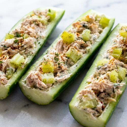 Keto Chicken Cucumber Boats with tangy dill pickles and monk fruit sweetener on a white marble surface.