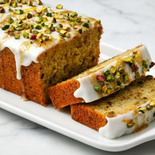 Lemon Pistachio Loaf with a brown butter and cardamom infusion on a white marble surface in soft natural lighting.
