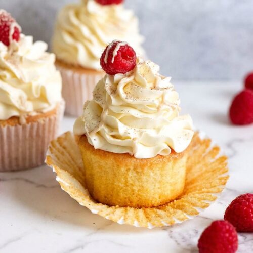 Frosted Vanilla Cupcakes with a malted vanilla infusion on a white marble surface under natural lighting.