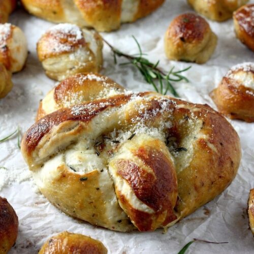 Golden Mozzarella Stuffed Rosemary Parmesan Soft Pretzels brushed with roasted garlic brown butter on a white marble surface.
