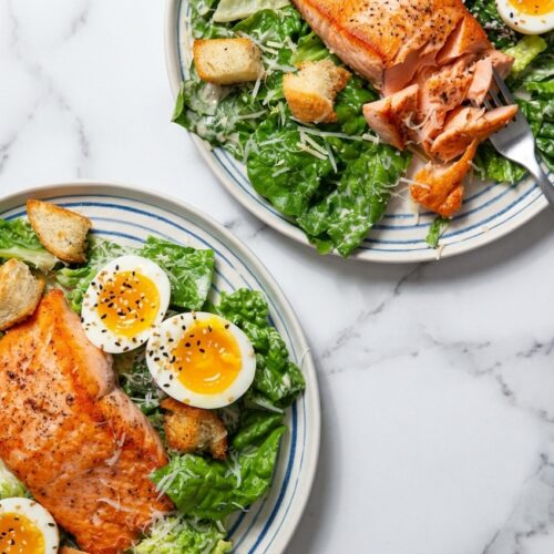 Salmon Caesar Salad With Hard Boiled Egg featuring a jammy egg coated in everything-bagel seasoning on a white marble surface.