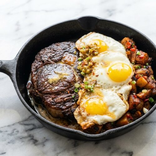 Seared Steak & Eggs with umami miso butter basting and sunny-side up eggs on a white marble surface.