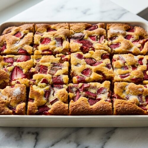 Strawberry Rhubarb Breakfast Cake with a golden ginger-sugar crust and brown butter on a white marble surface.