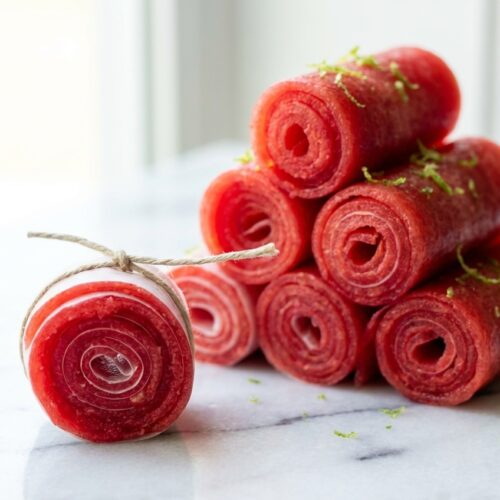 Vibrant Watermelon Fruit Roll Ups with lime zest and citric acid on a minimalist ceramic plate over white marble.